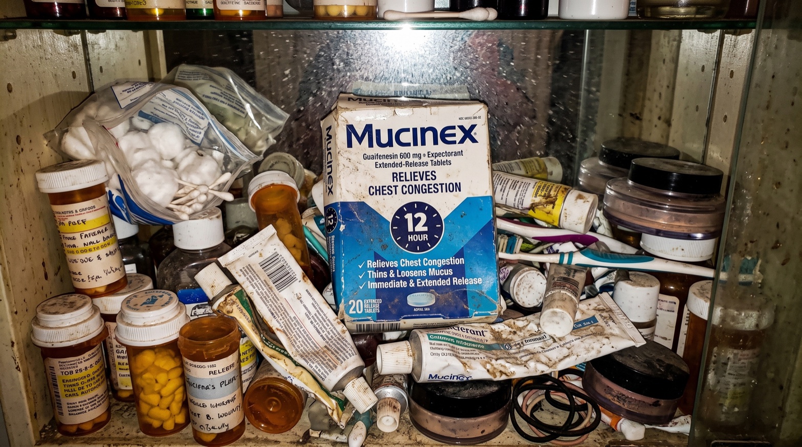 A Mucinex 12 Hour box on a bathroom sink counter in morning light, next to a glass of water
