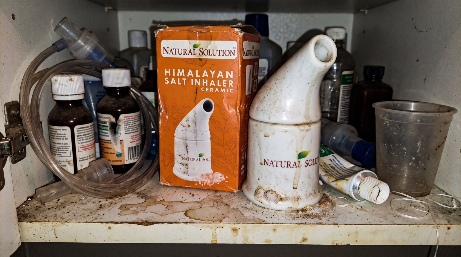 A grubby ceramic Himalayan salt inhaler and its worn box shoved in the back of a cluttered bathroom cabinet